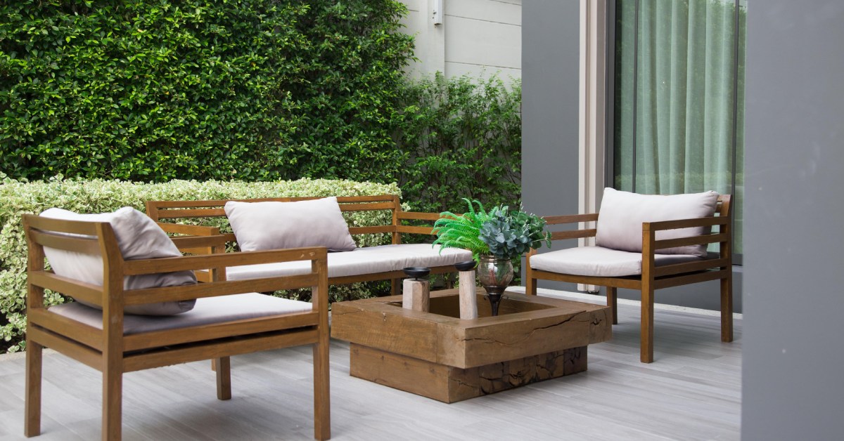 An outdoor living space in a home’s backyard with reclaimed wood furniture and bushes in the background.