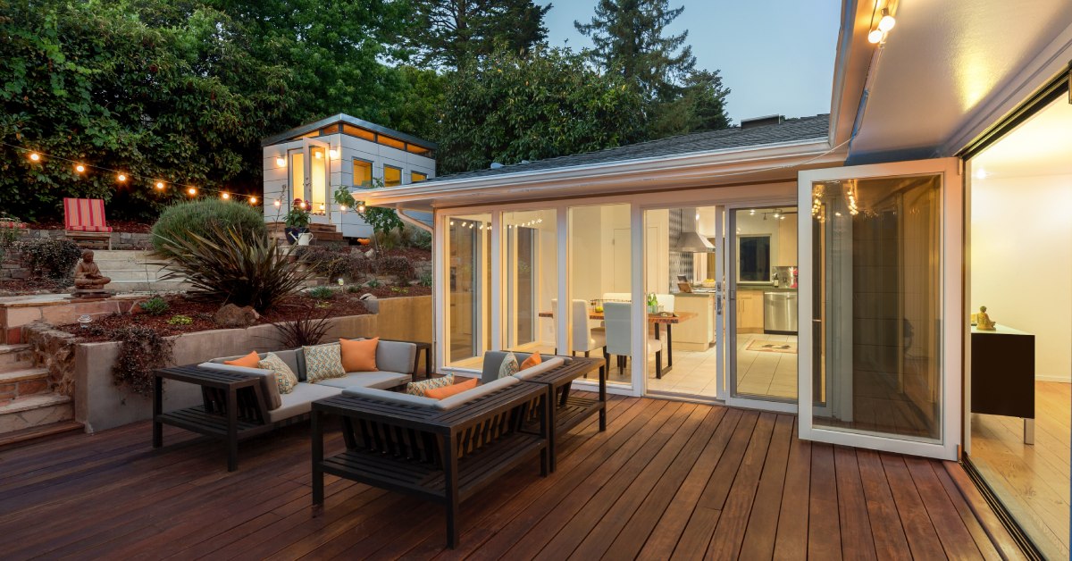 A luxurious outdoor deck with a sitting area, built-in planters, string lights, and views into the kitchen and living room.